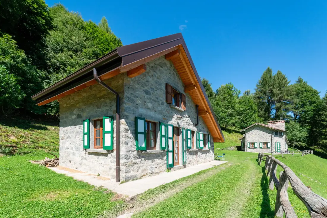 Una casa de piedra con ventanas de bordes verdes está junto a un patio de césped.