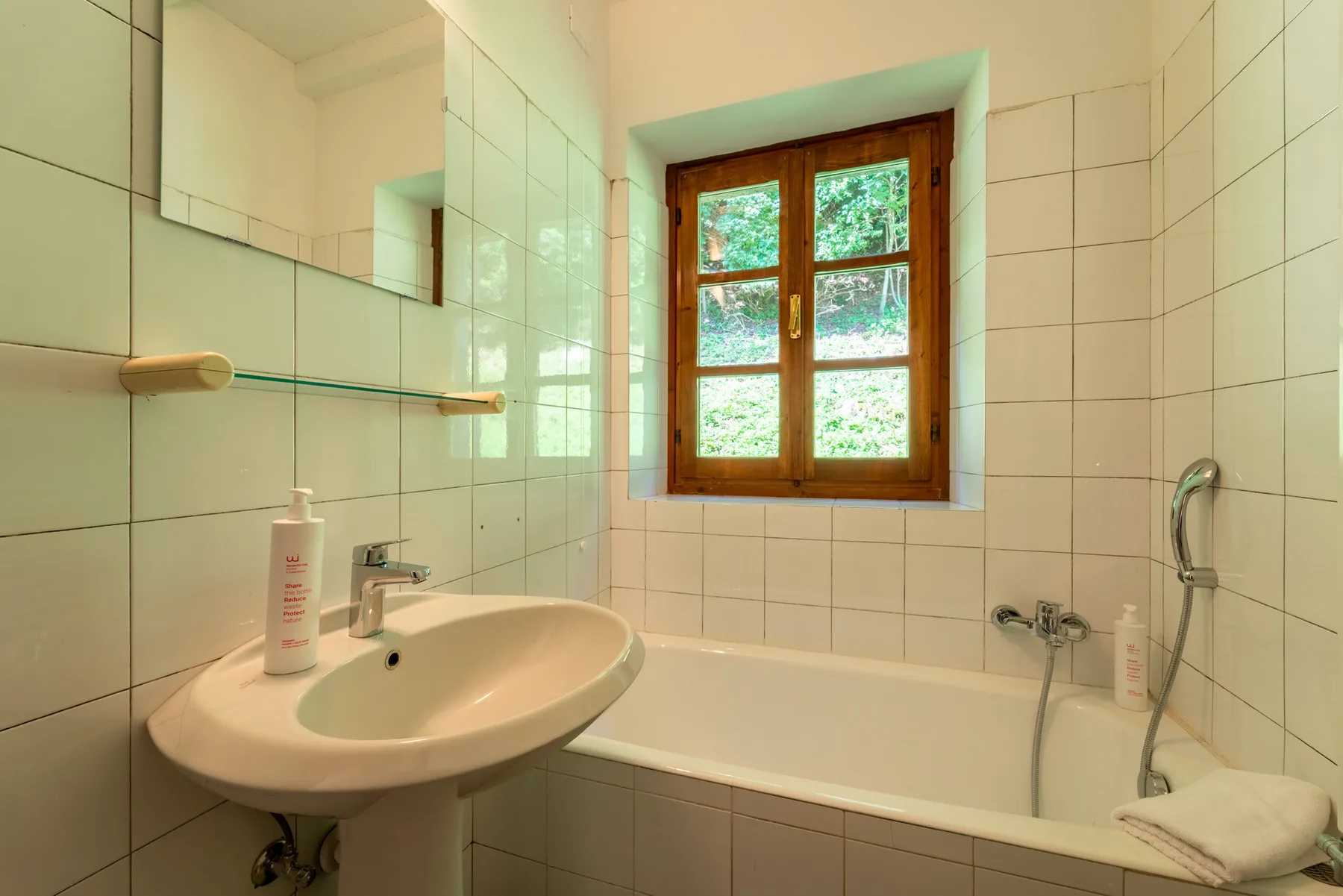 Un baño con azulejos, lavabo, bañera y una ventana con marco de madera.