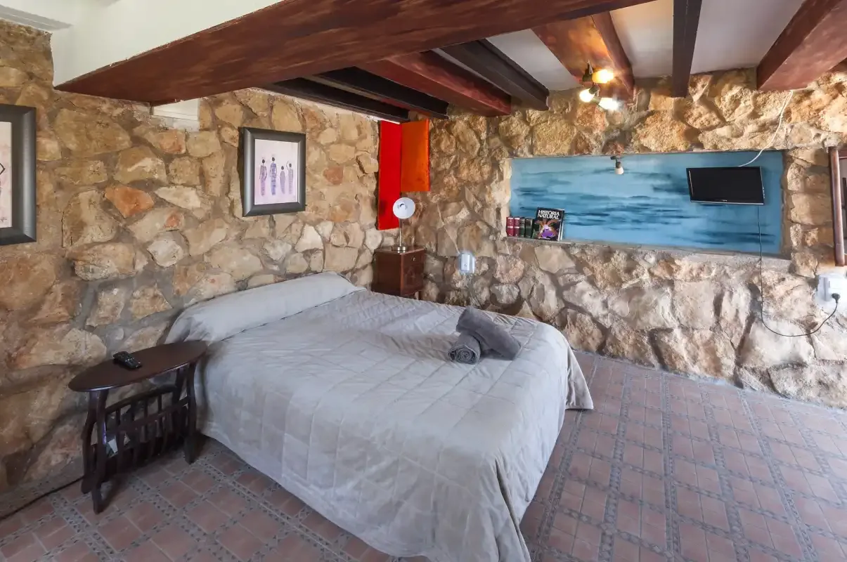 A bedroom with a bed beneath exposed wooden beams and stone walls.