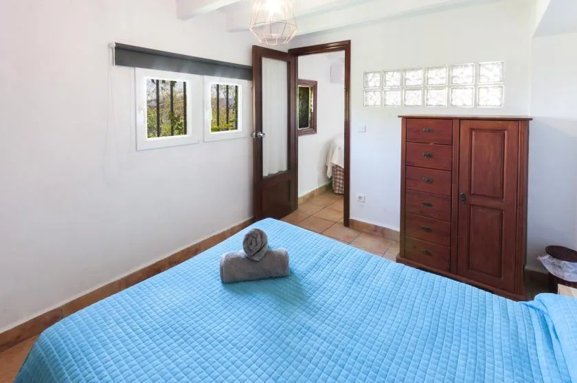 A bedroom with a blue quilted bedspread and a wooden wardrobe.