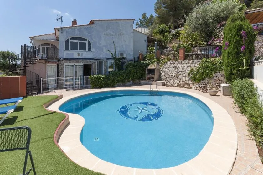 An outdoor swimming pool sits beside a house and landscaped stone wall.
