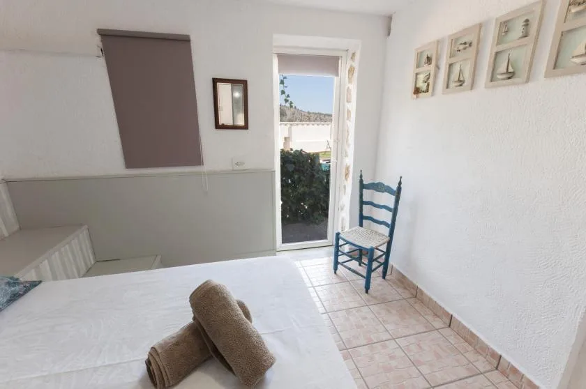 A bright bedroom with a bed, tiled floor, and a glass door opening to a balcony.