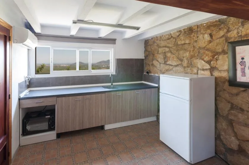 A compact kitchen with a long counter, windows, and a refrigerator.