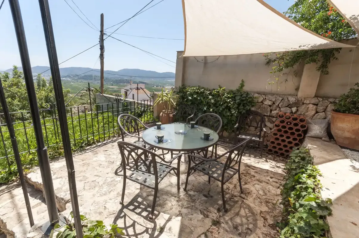 An outdoor patio has a round table and seating beneath a shade canopy.