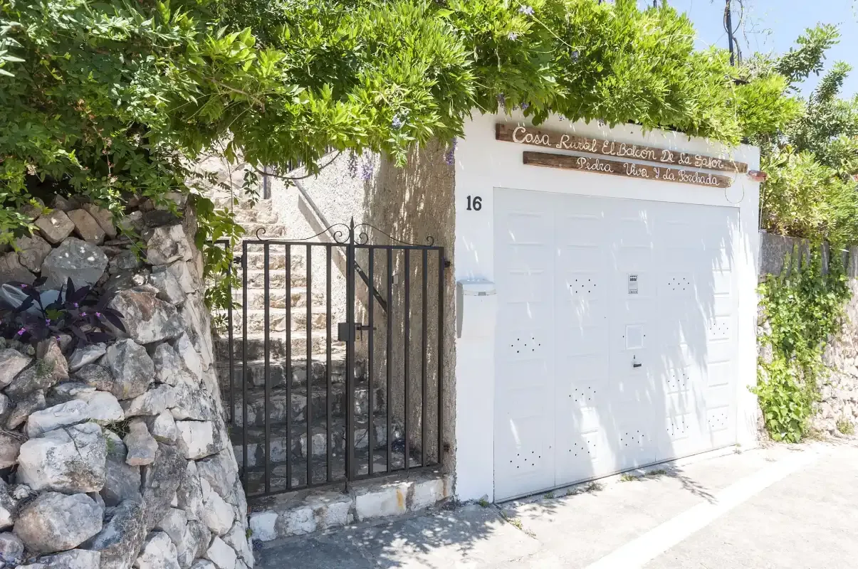 A gated entrance beside a white garage door, partly shaded by leafy branches.