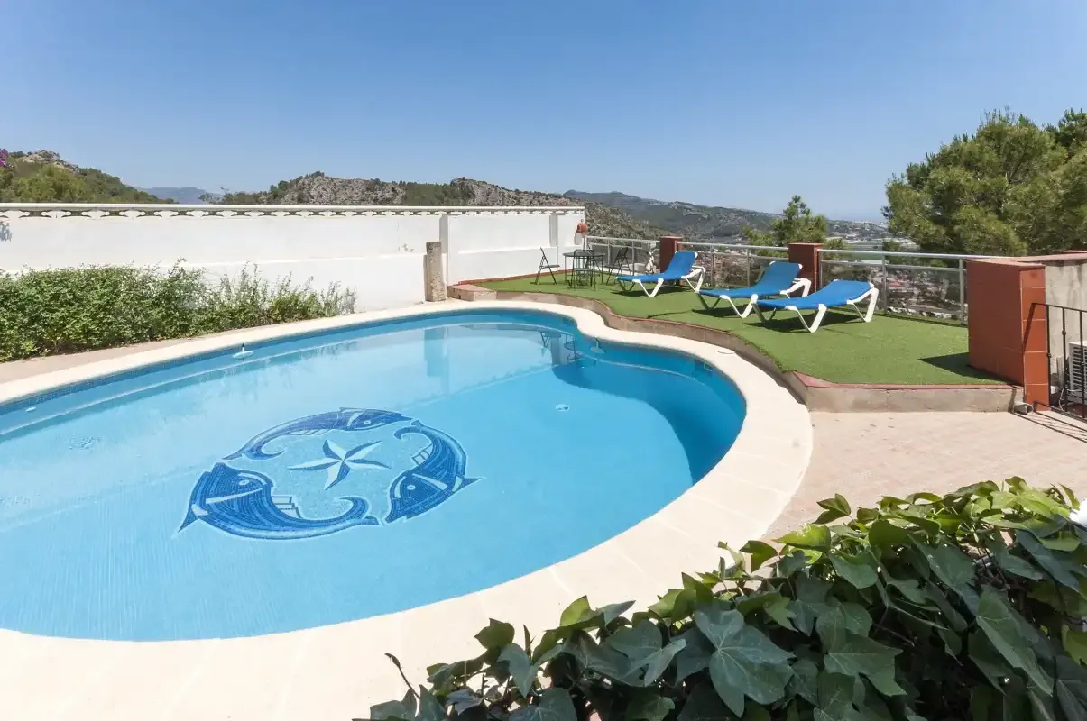 A swimming pool beside a sun terrace with lounge chairs and distant hills.