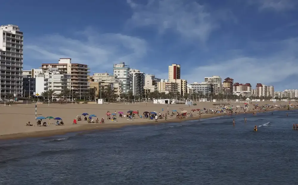 A city beach with people along the shoreline and apartment buildings behind it.