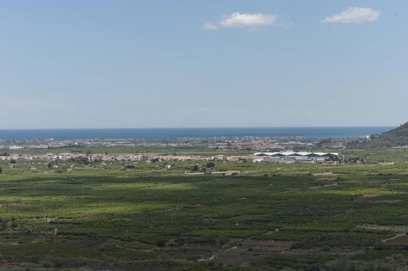 A broad green landscape stretches toward a coastal town and the sea.