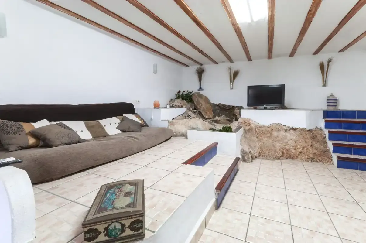 A living room with tiled floors, a long seating area, and a television.