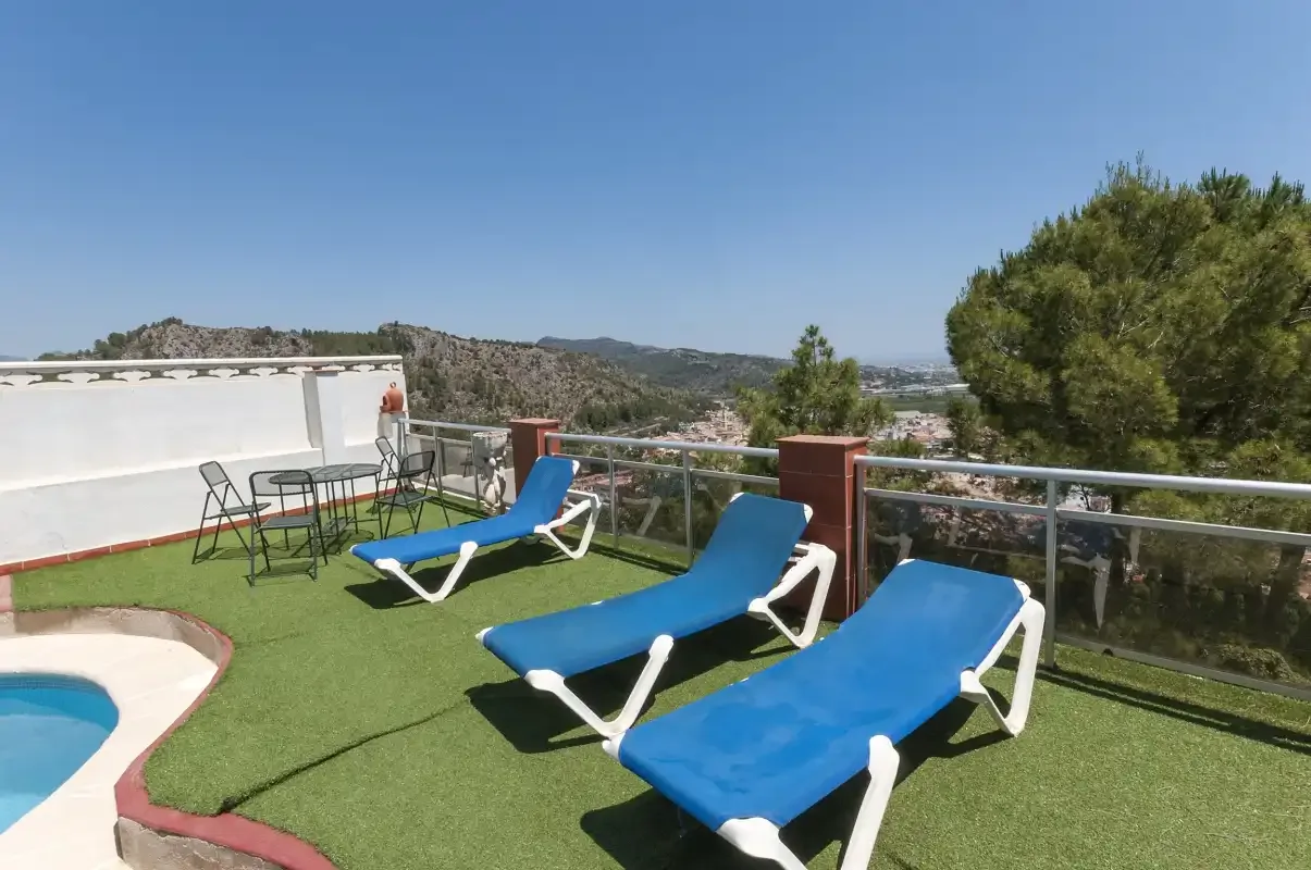 A rooftop terrace has blue lounge seating beside a small pool and railing.