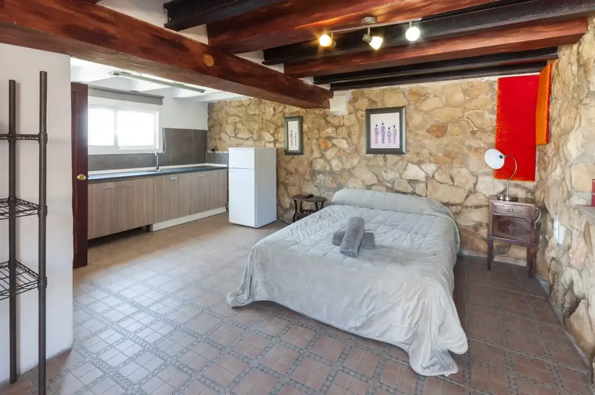 A bedroom with a bed, stone walls, and a compact kitchen area.