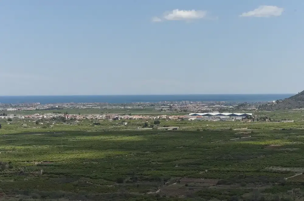 A broad green plain stretches toward a coastal town and the sea.