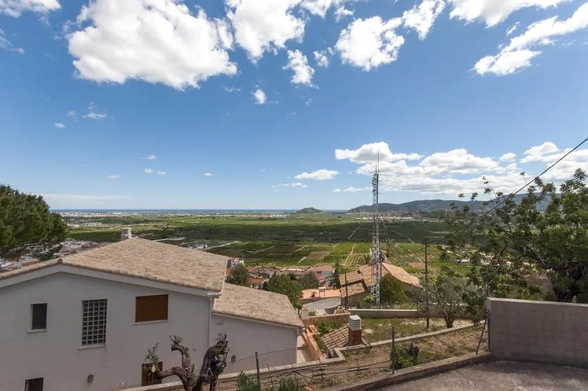 A hillside view overlooks houses, green fields, and distant hills beneath a cloudy sky.