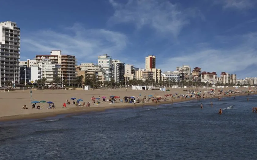 A sandy urban beach with people along the shore and apartment buildings in the background.