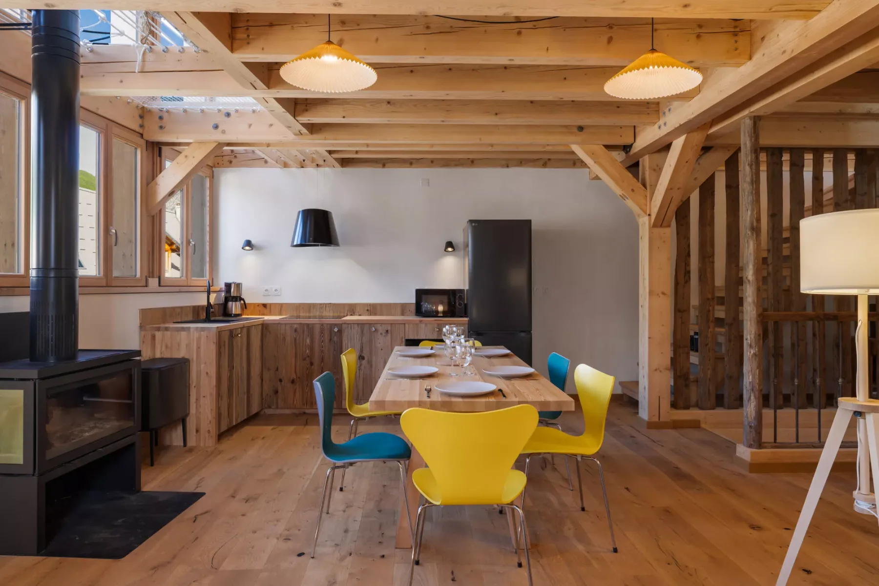 A rustic dining area with a wooden table, colorful seating, and exposed beams.