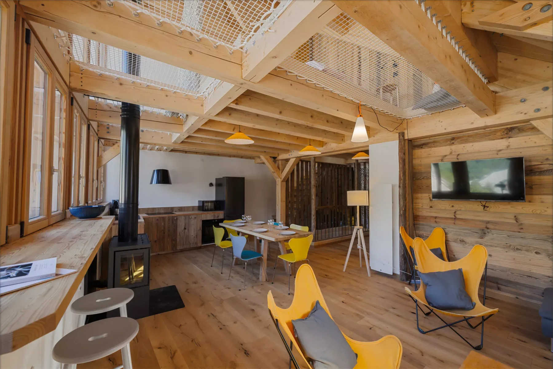 Un salón revestido de madera con asientos de colores, una mesa de comedor y un televisor en la pared.