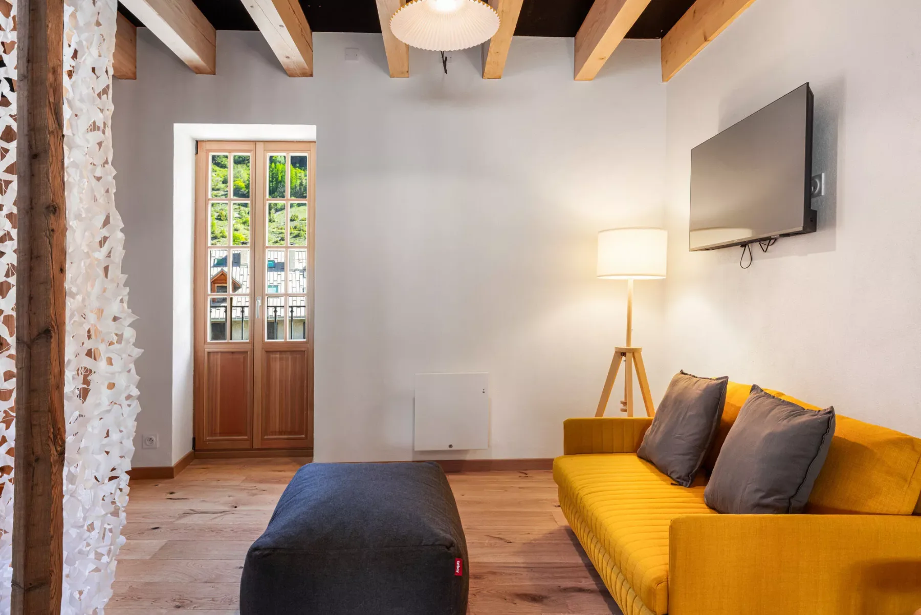 Una sala de estar con sofá amarillo, otomana oscura y televisor.