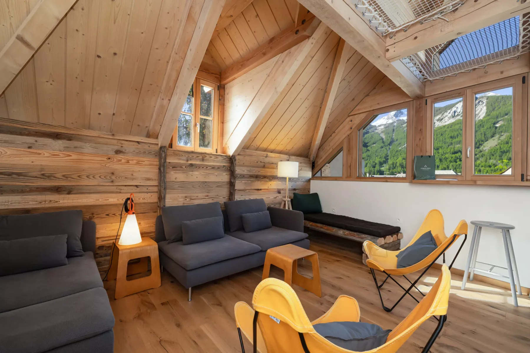 A wood-paneled living room with seating and large windows overlooking green hills.