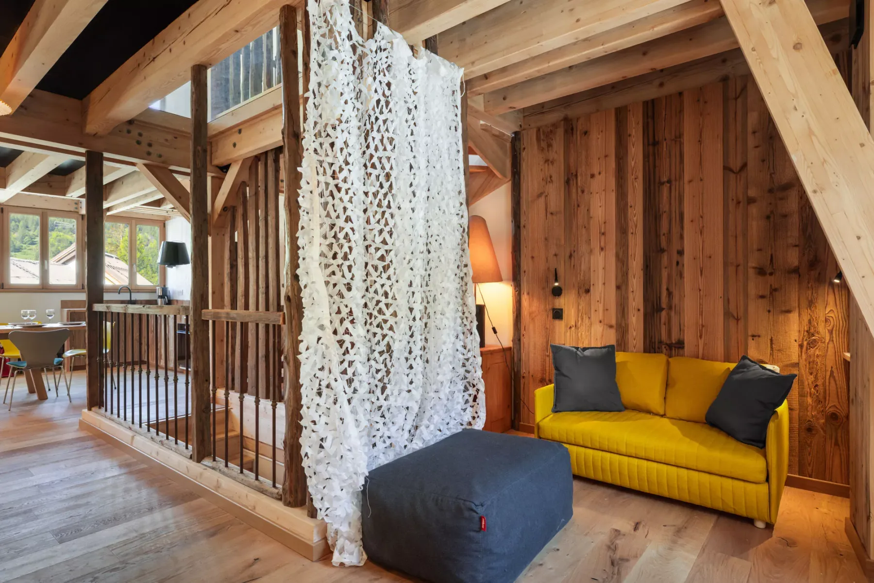 Una sala con paredes de madera tiene un sofá amarillo y un separador blanco colgante.