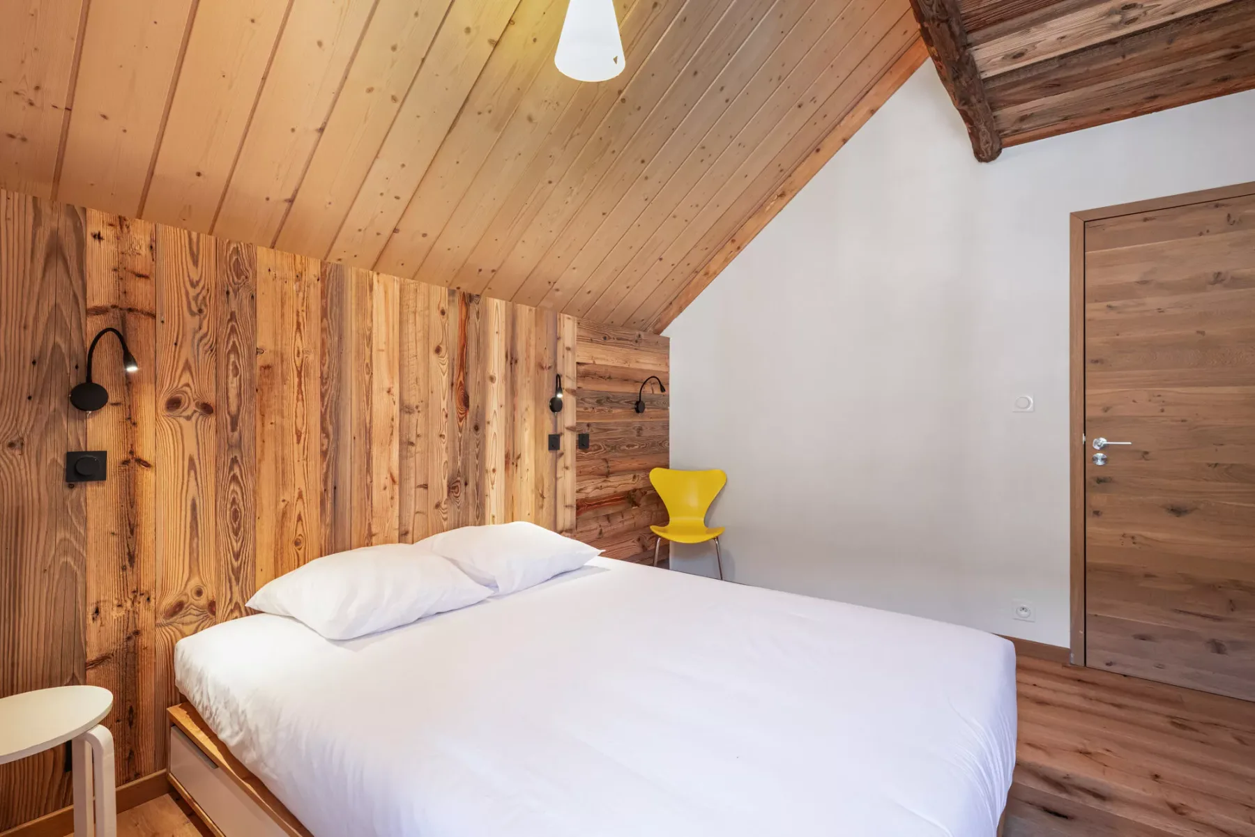 Un dormitorio con una cama, paredes revestidas de madera y un techo inclinado de madera.