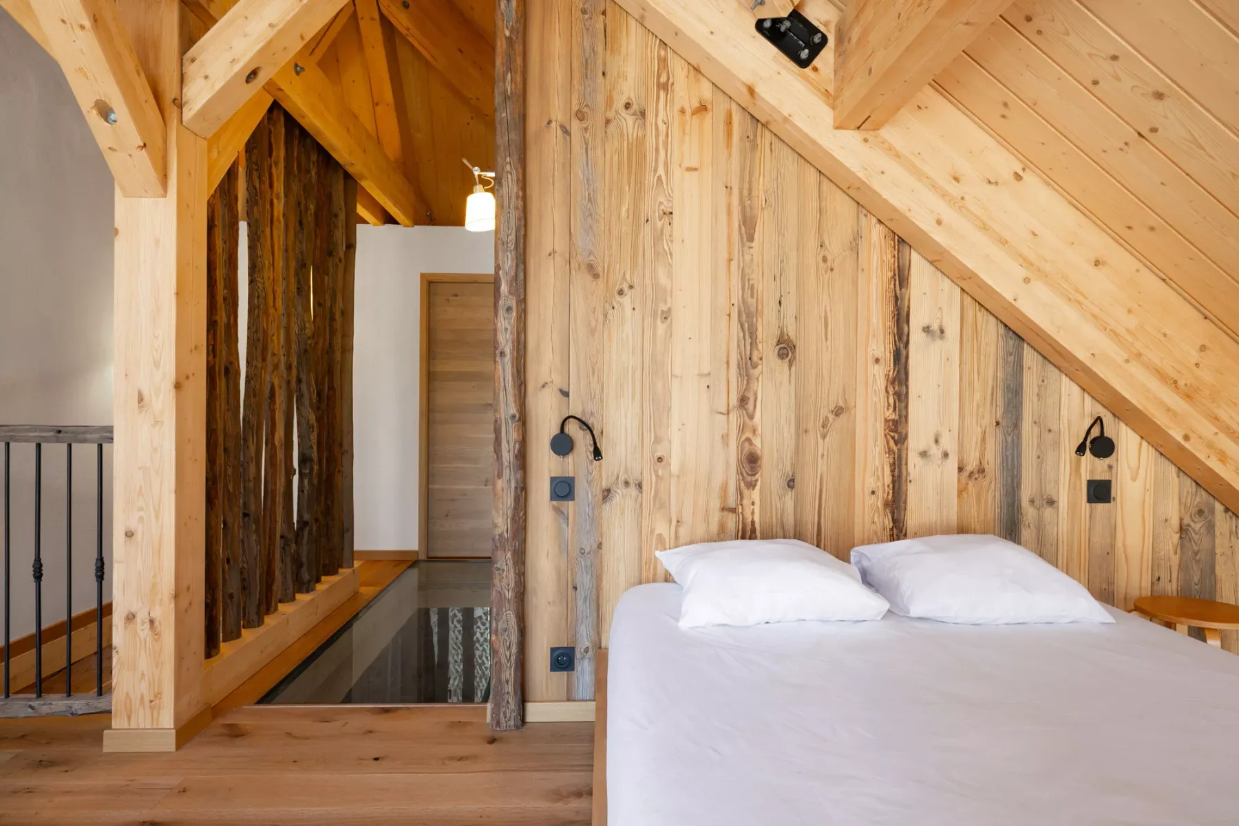 Una cama queda bajo un techo inclinado revestido de madera, junto a un pasillo estrecho.