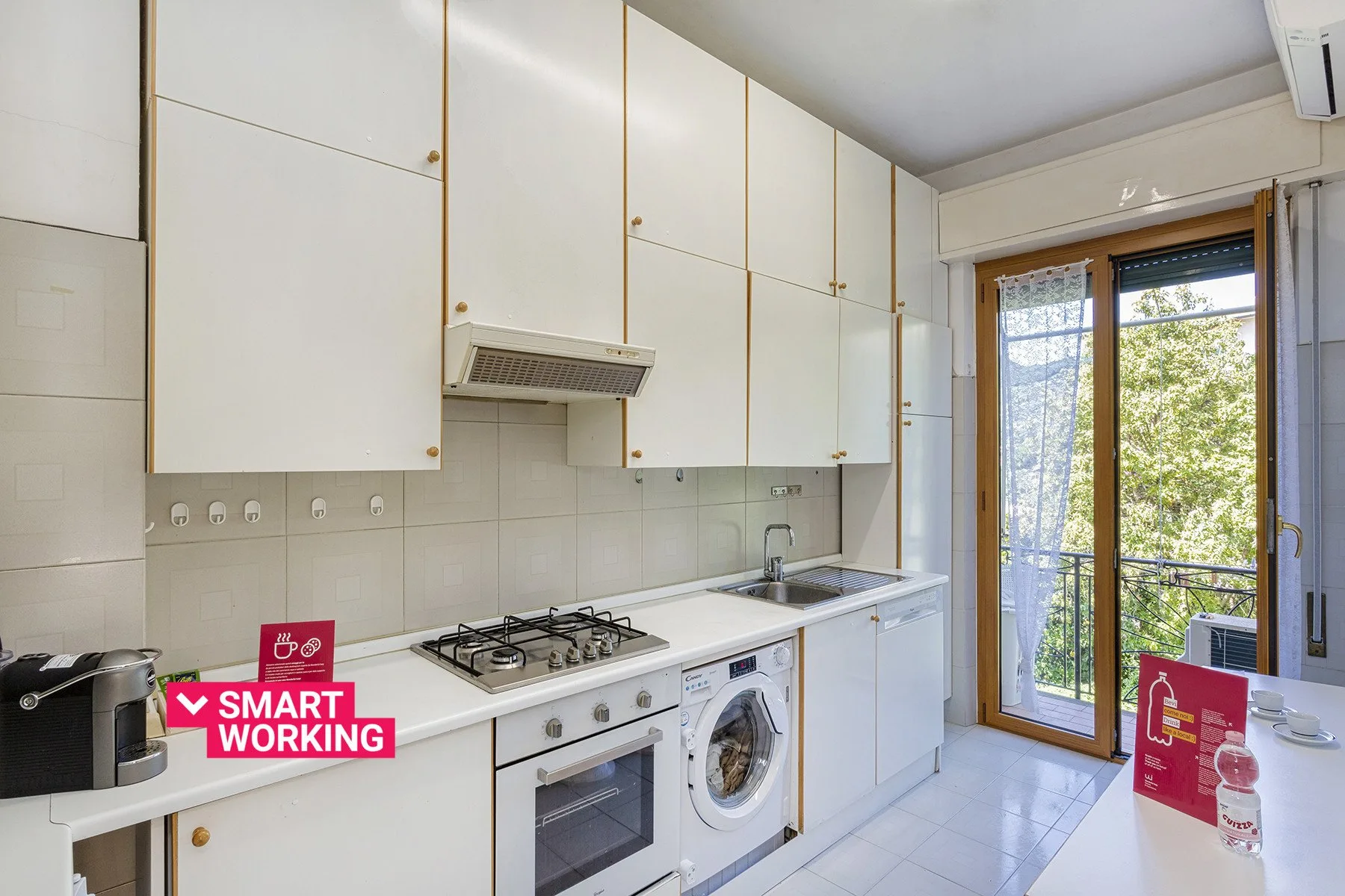 Una cocina luminosa con armarios blancos, una placa de cocina y un fregadero junto a una puerta al balcón.