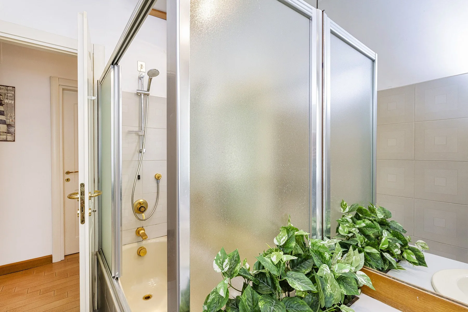 Un baño con una ducha de vidrio esmerilado y plantas frondosas junto al lavabo.