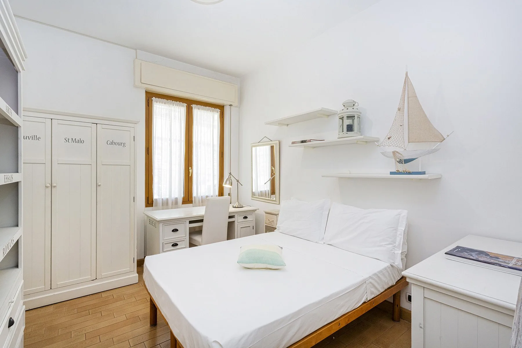 Un dormitorio luminoso con una cama, muebles blancos de almacenamiento y una ventana.