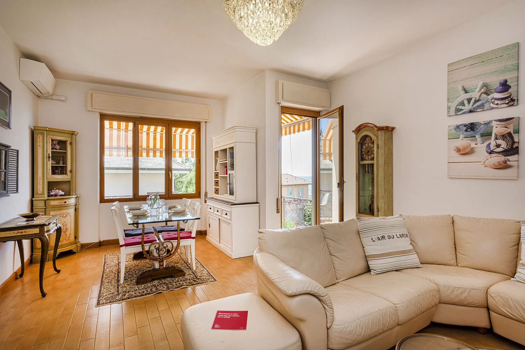 Una sala luminosa con una zona de estar color crema y una mesa de comedor junto a las ventanas.