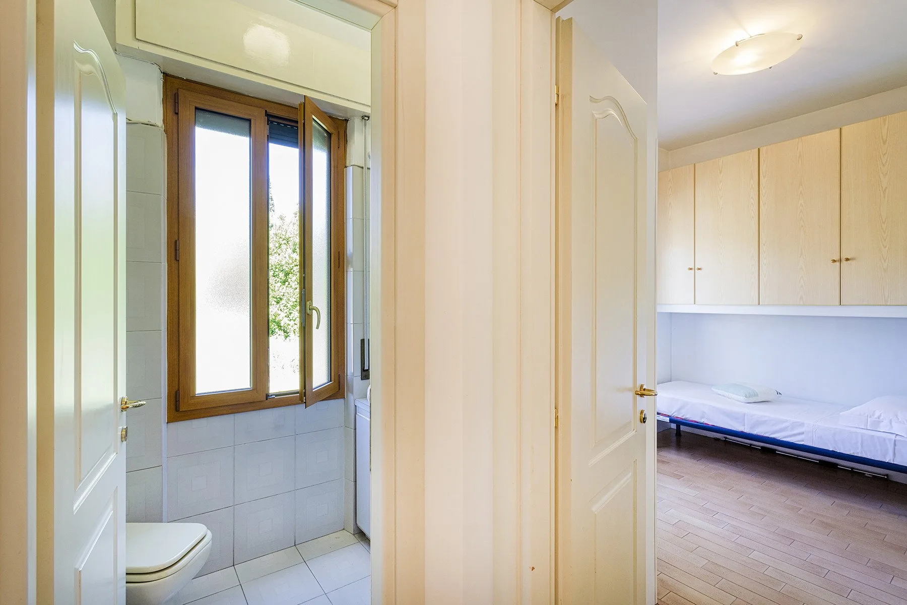 Un pasillo da a un baño con azulejos y a un dormitorio con una cama.