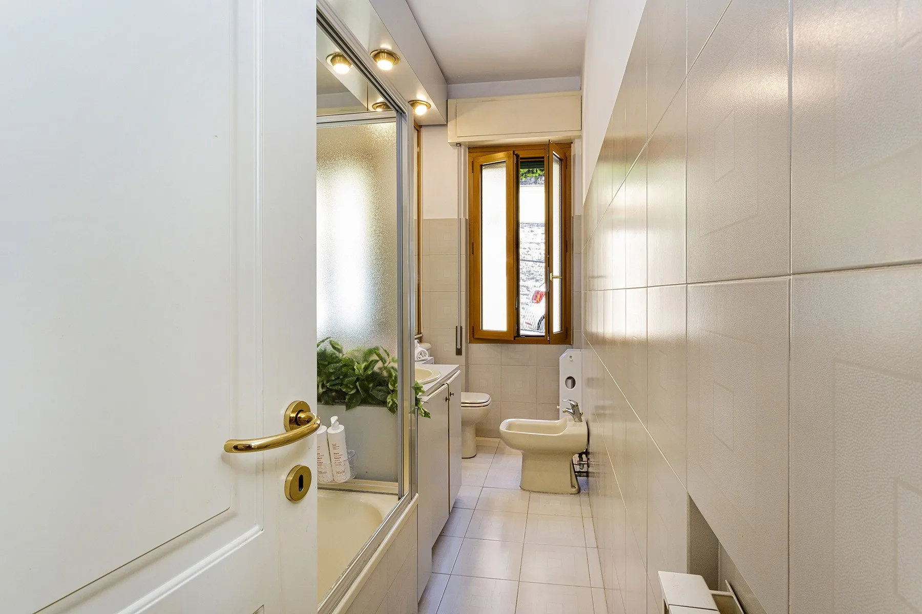 Un baño alicatado con bañera, inodoro y una ventana estrecha.