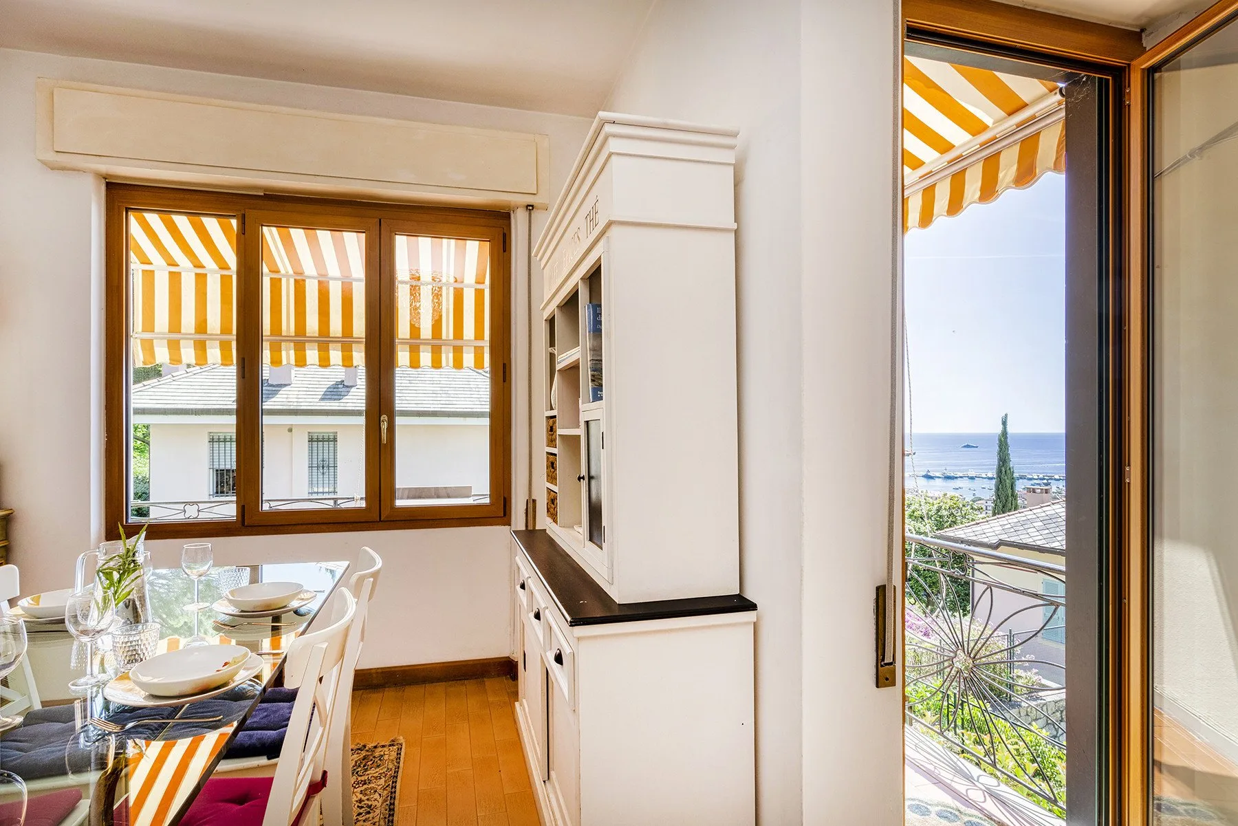 Comedor con una mesa junto a una ventana y una puerta abierta al balcón.