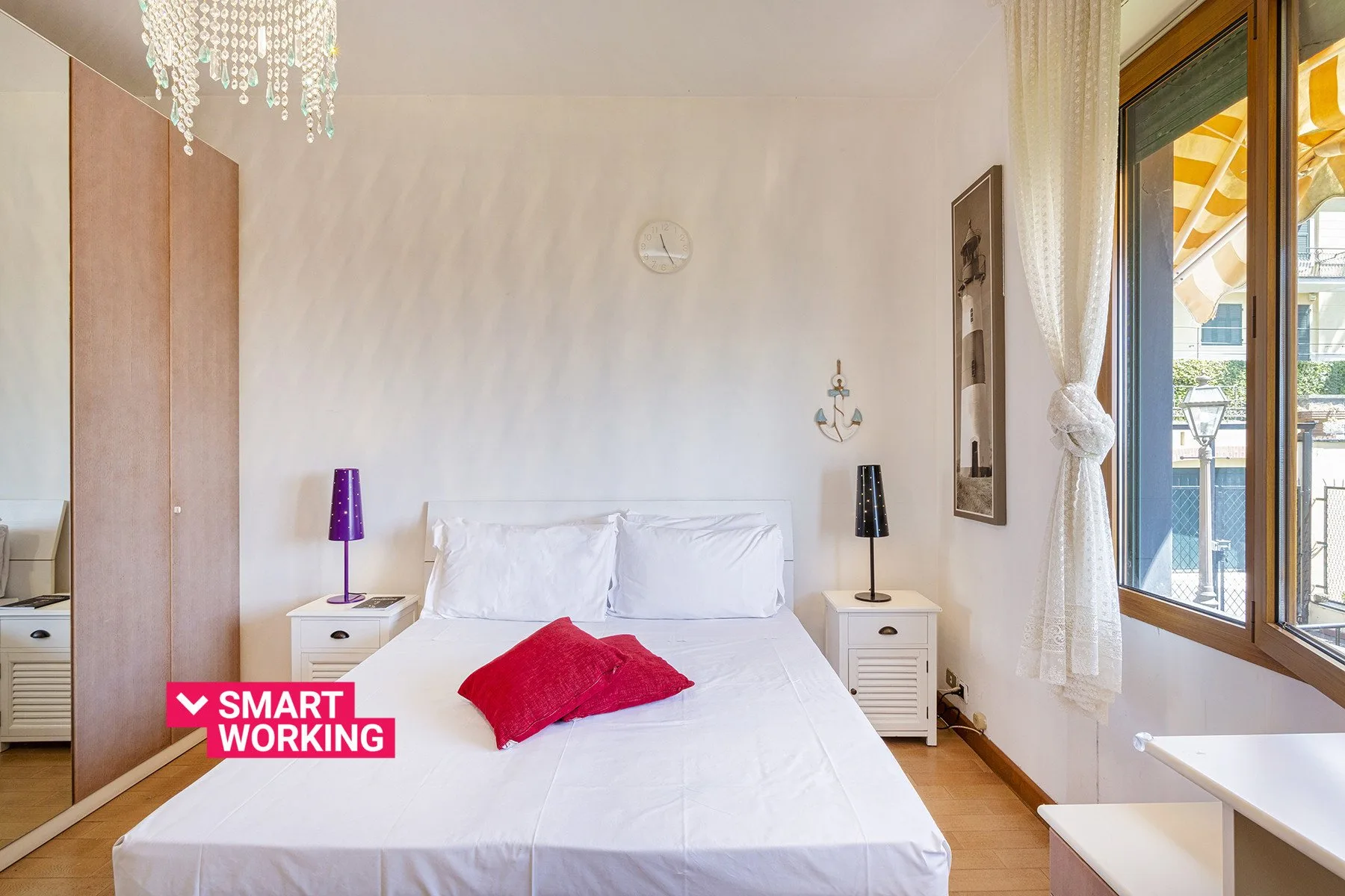 Un dormitorio con una cama blanca, mesitas de noche y una ventana grande.