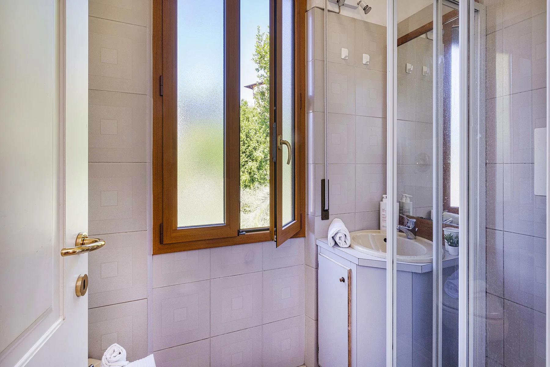 Un baño luminoso con ventana, lavabo y ducha de vidrio.