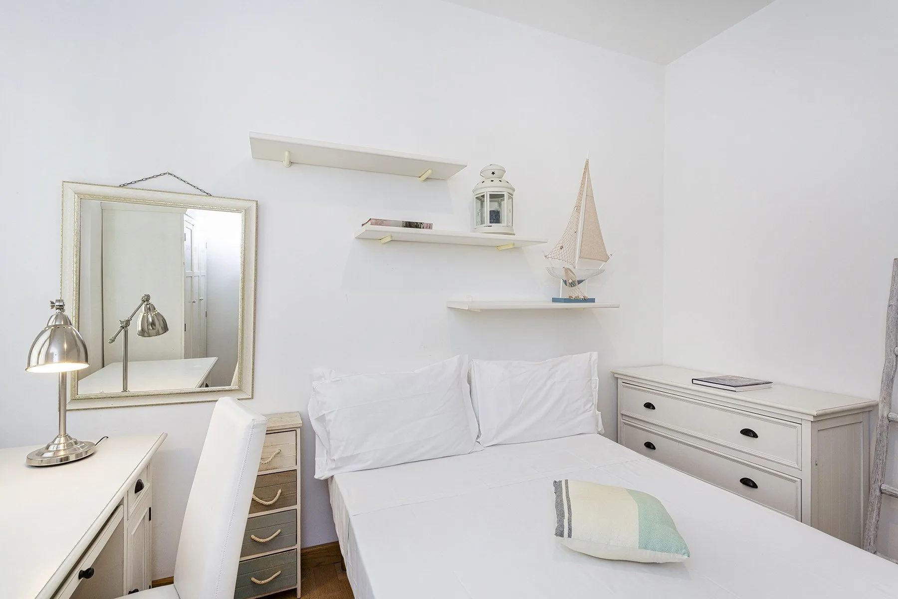 Un dormitorio luminoso con una cama blanca y estantes sencillos en la pared.