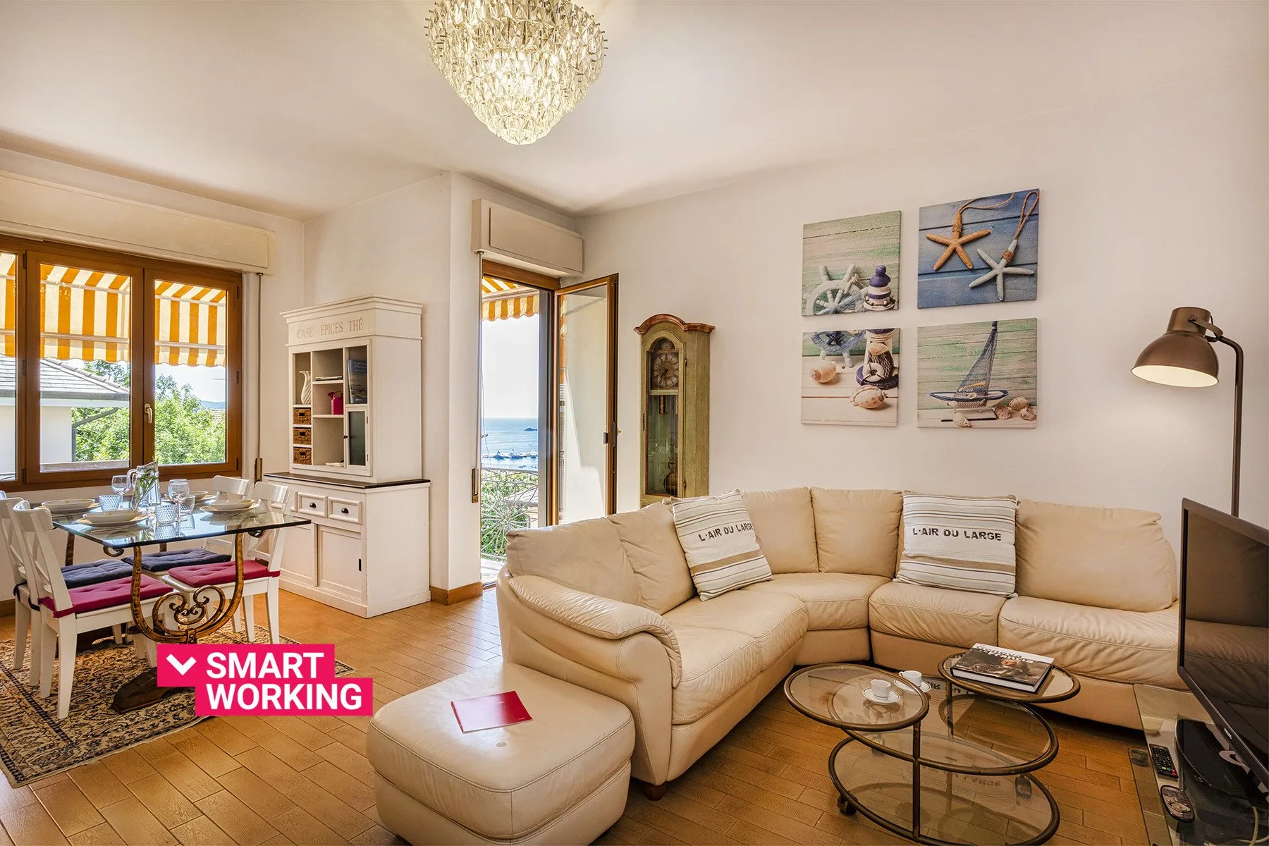 Una luminosa sala de estar con asientos beige, una mesa de centro de vidrio y ventanas con vistas al agua.