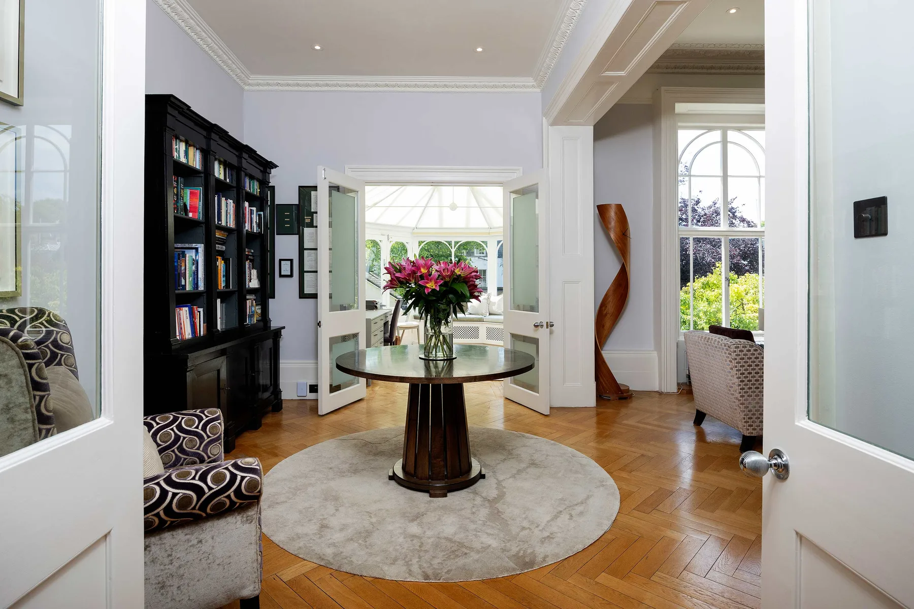 Una sala luminosa con una mesa redonda, flores y estanterías.