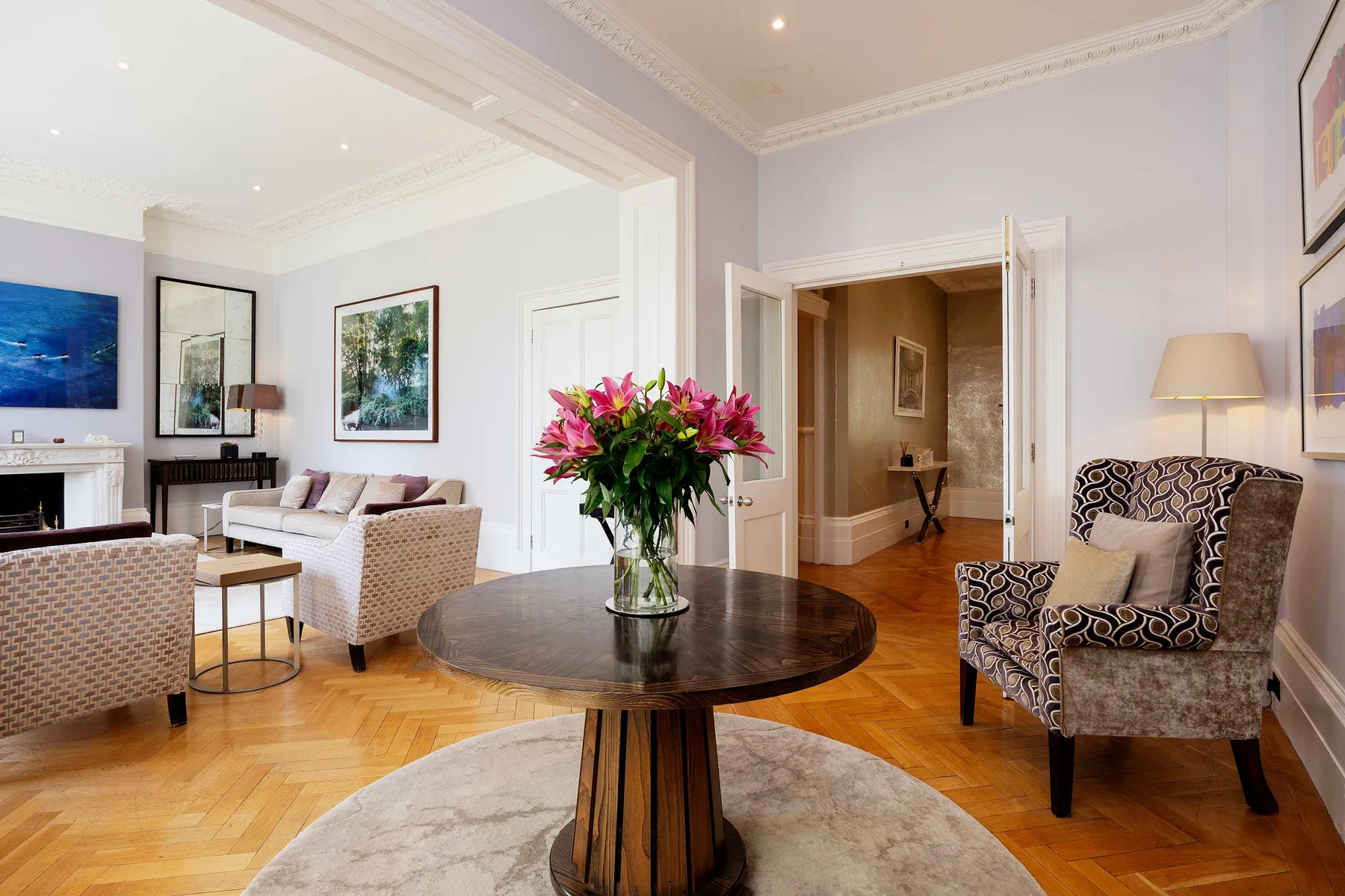 A bright living room with seating, a round table, and a vase of flowers.