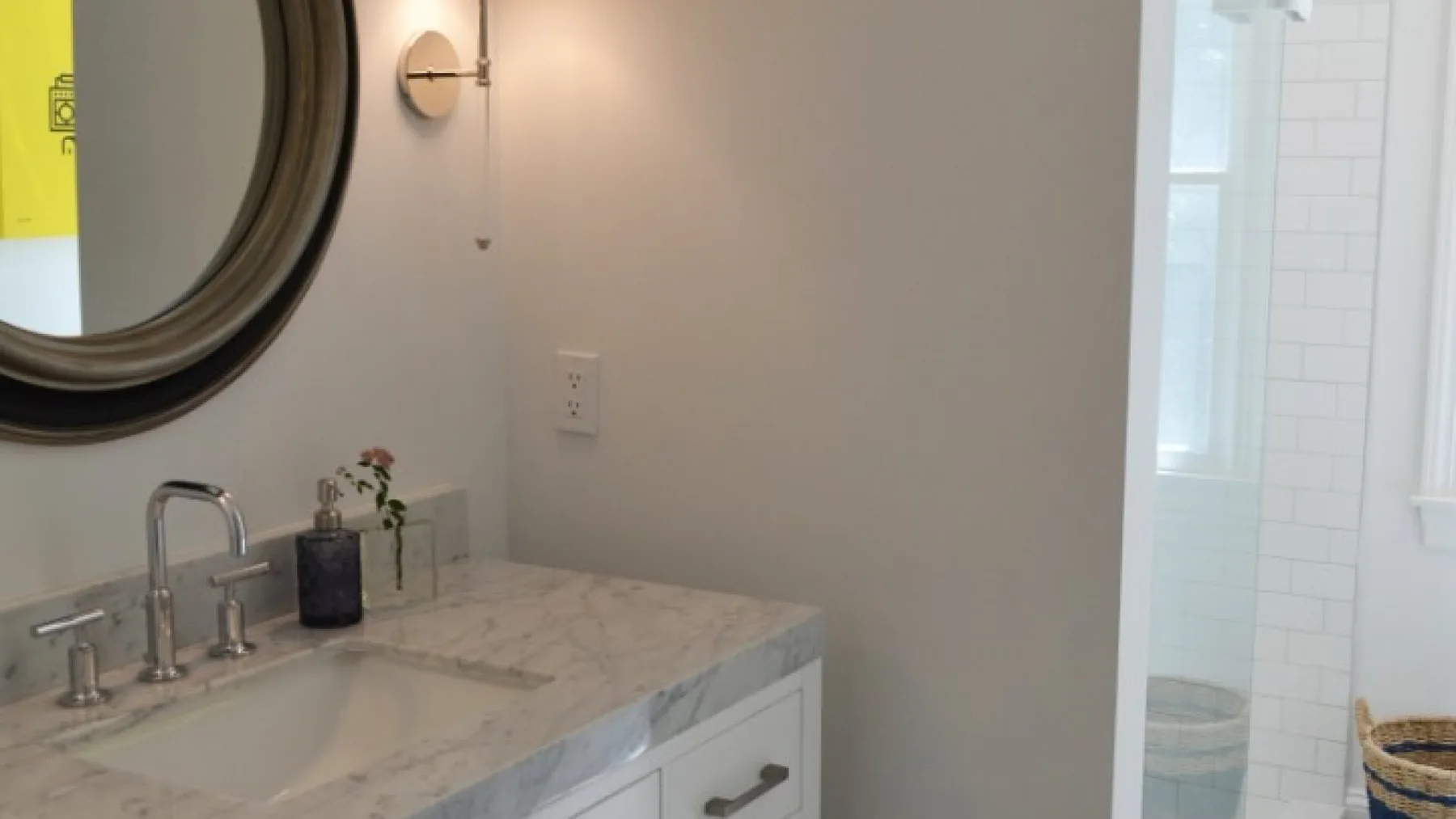 Un lavabo de baño con espejo redondo está junto a una ducha alicatada.