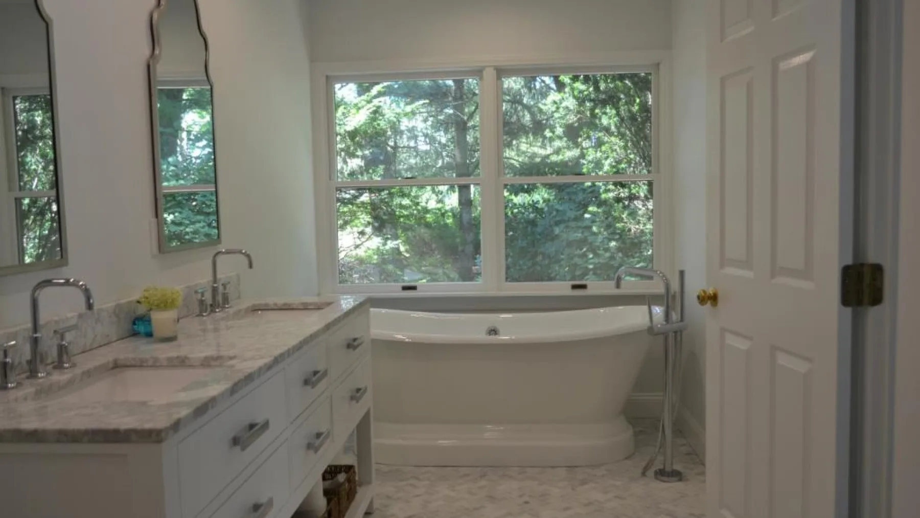 Un baño luminoso con una bañera bajo ventanas amplias y un lavabo con encimera.