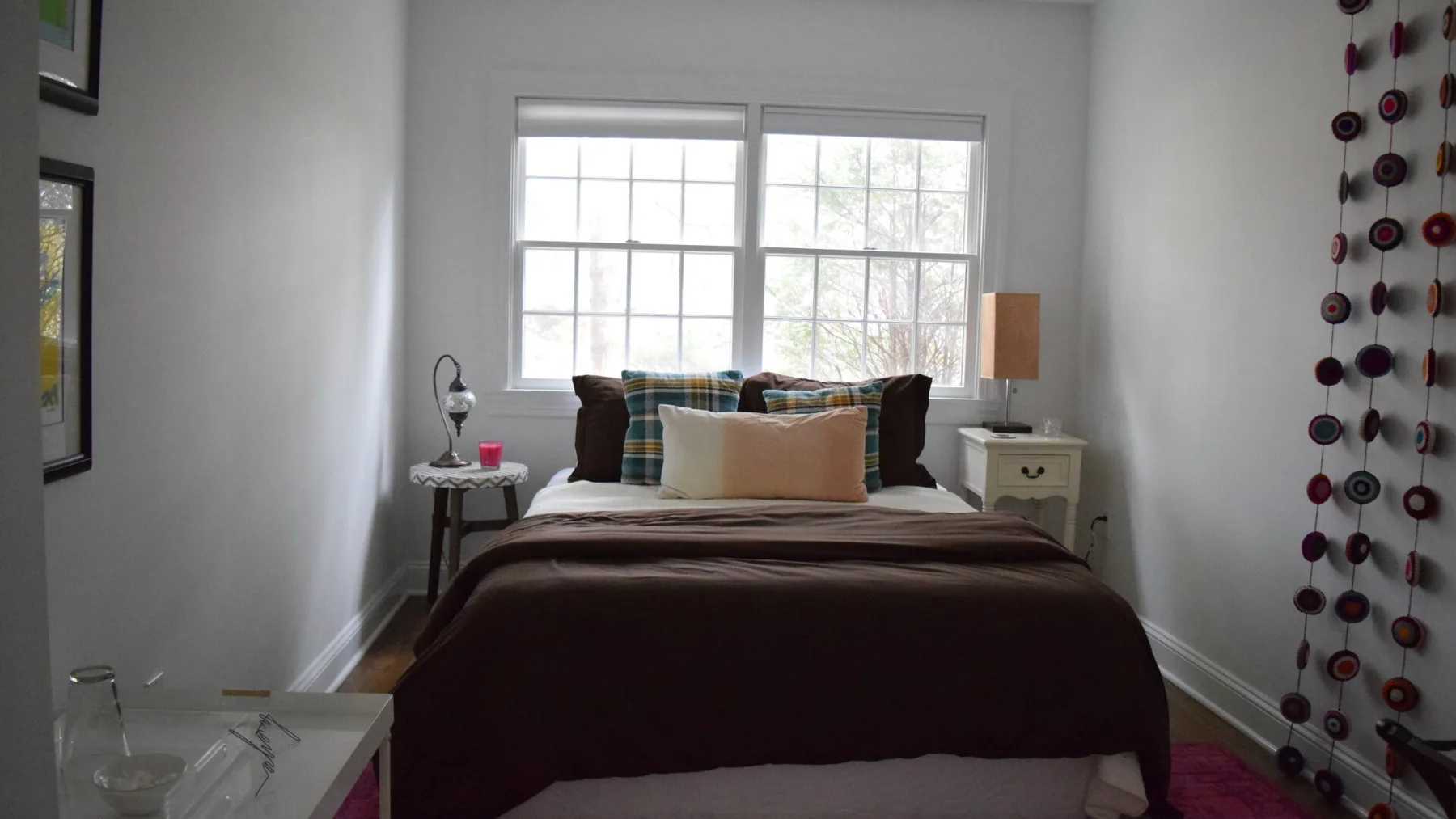 Un dormitorio con una cama bajo dos ventanas y mesitas de noche.