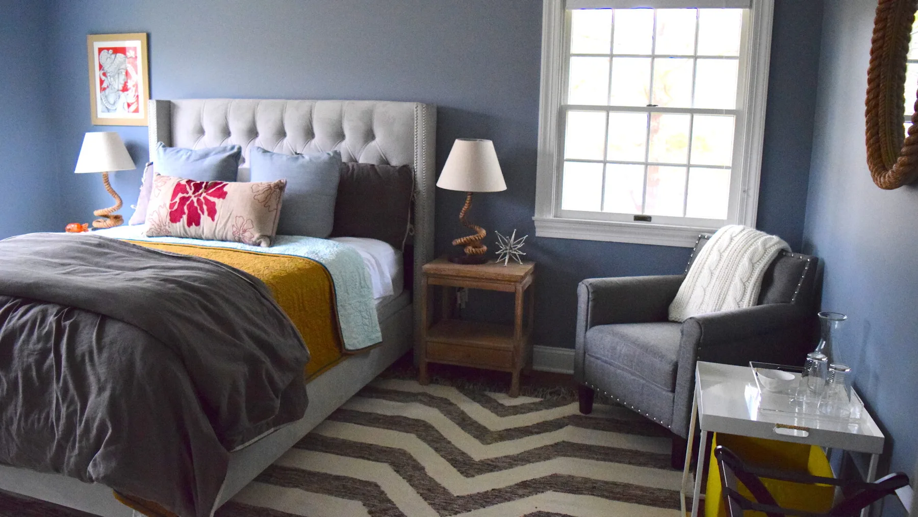 Un dormitorio con una cama, un sillón gris y una alfombra con diseño de espiga.