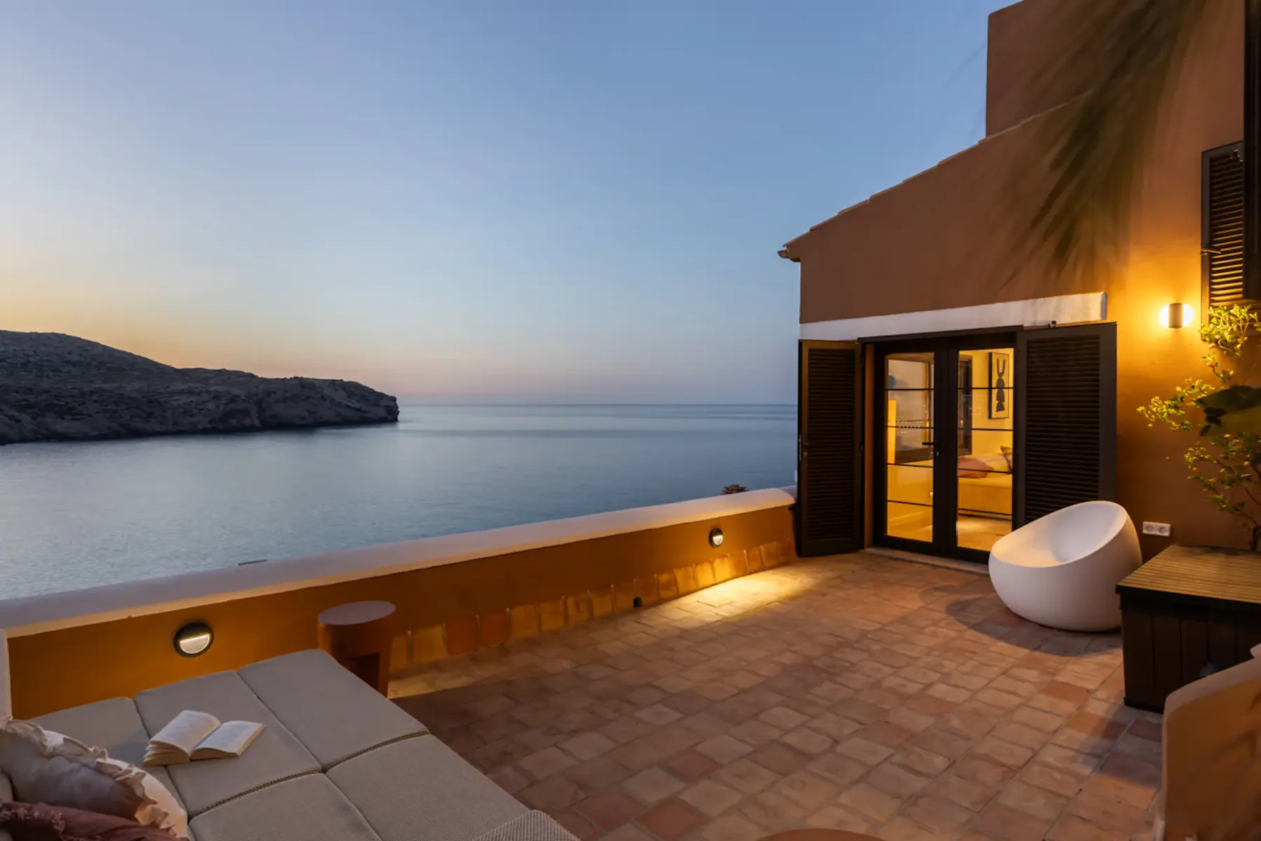 A seaside terrace at dusk with seating and a calm ocean view.