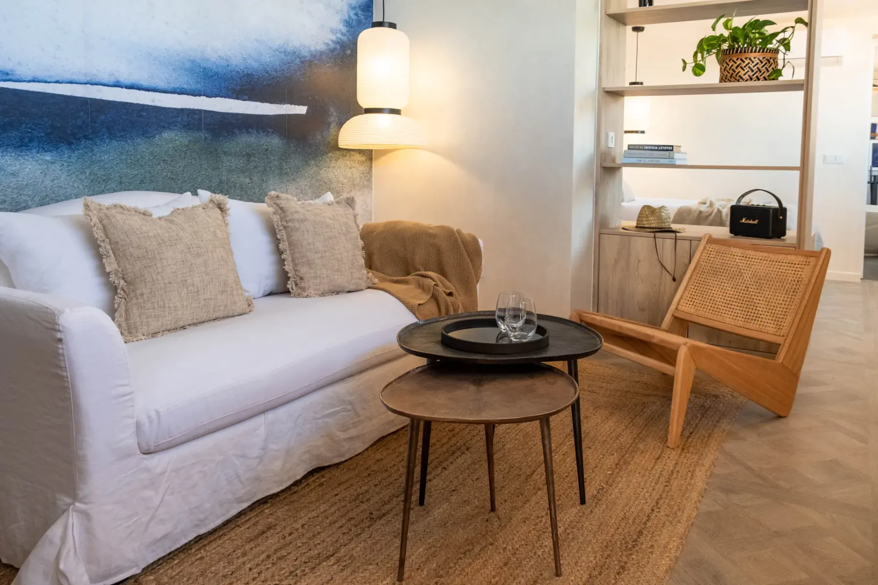 A living room with a white sofa, coffee tables, and a wooden lounge chair.