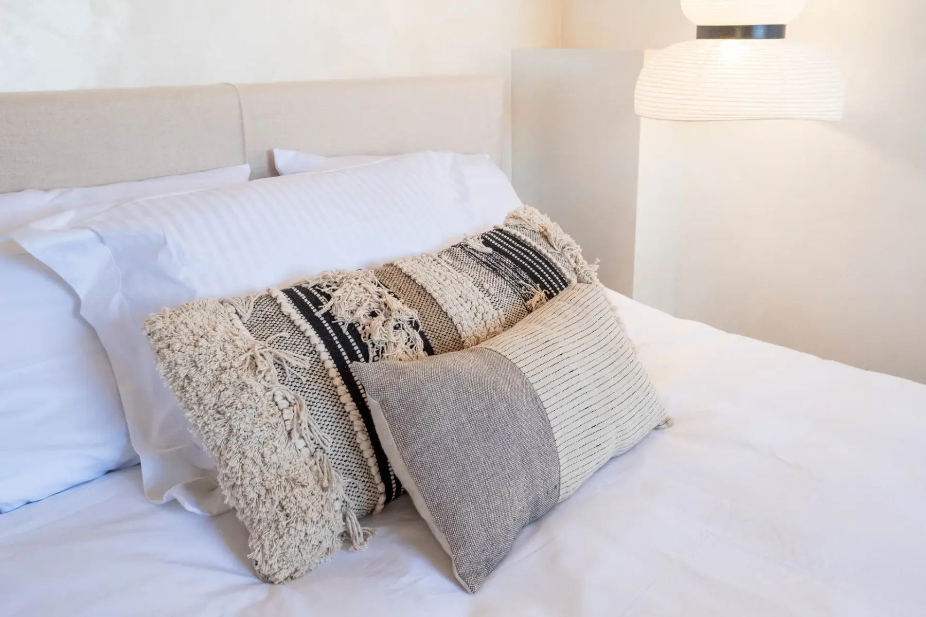 A neatly made bed with white linens and textured decorative pillows.