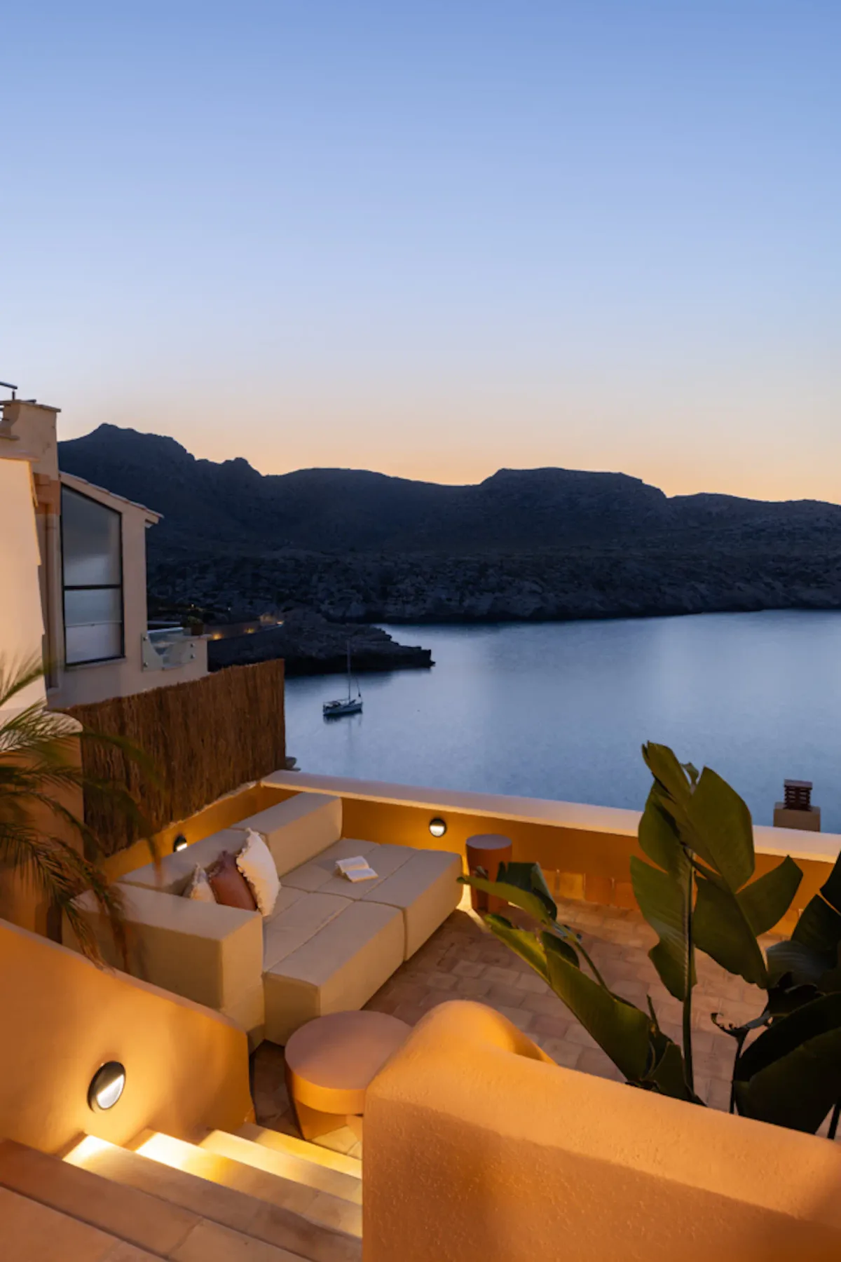 A terrace overlooks a calm bay and dark mountain silhouettes at dusk.