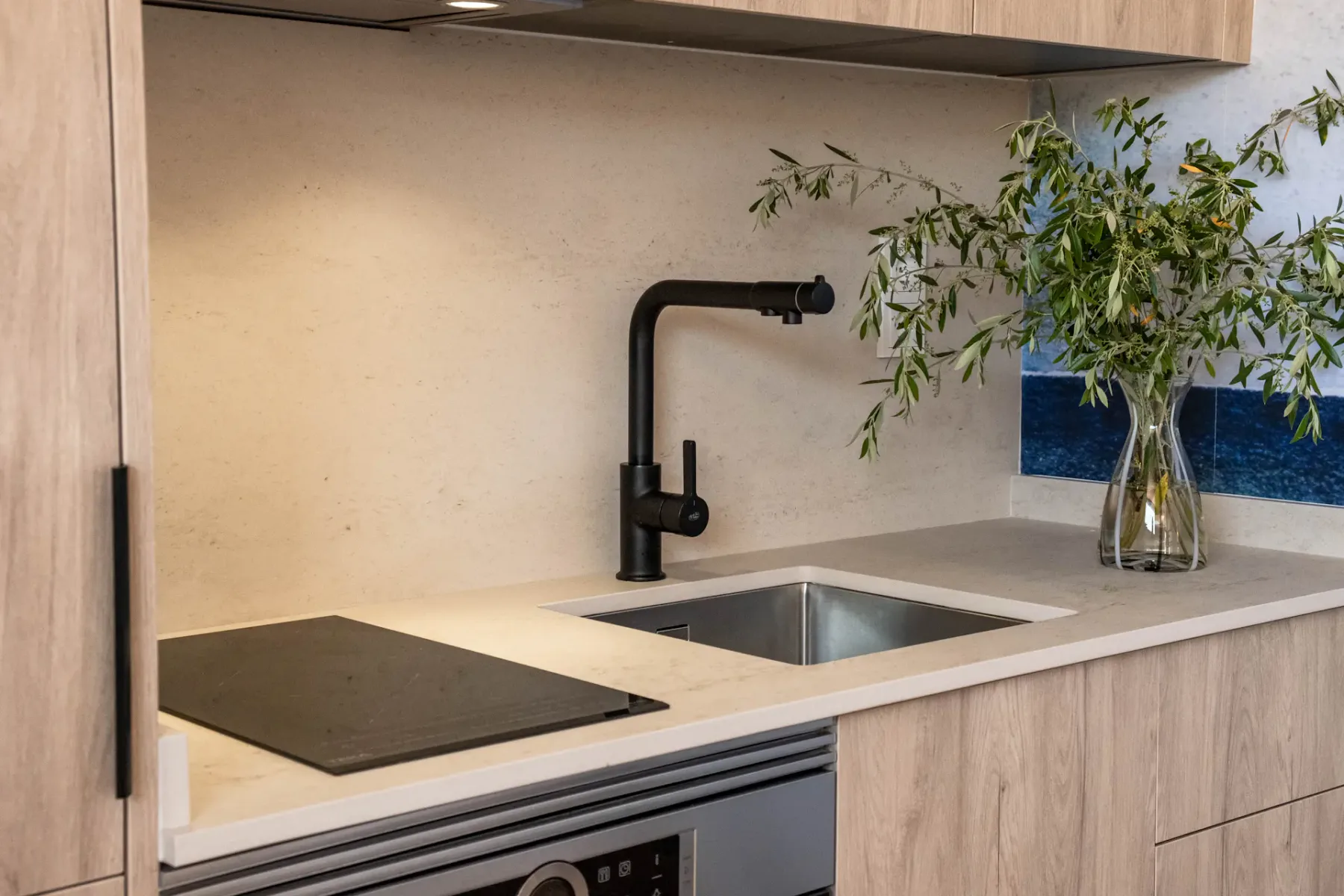 A kitchen countertop with a sink, faucet, and black cooktop.