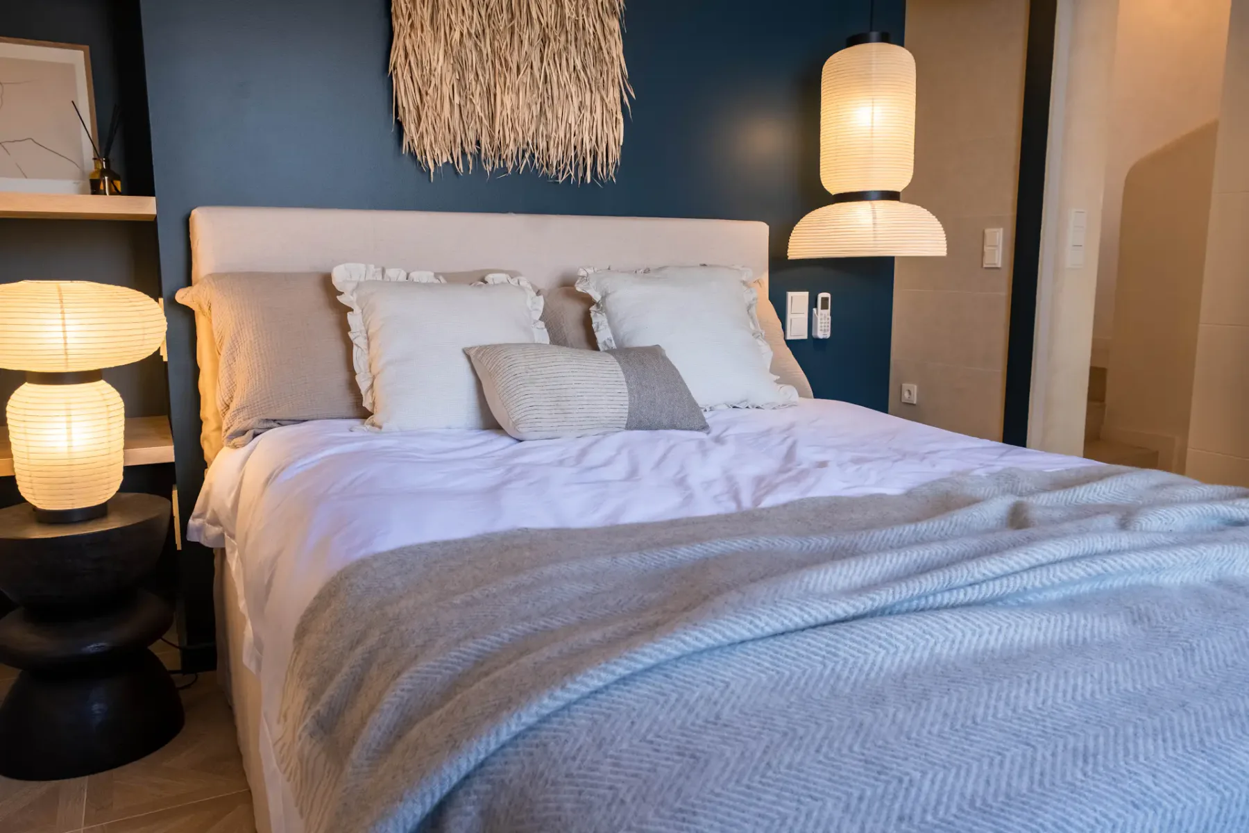 A bedroom with layered white bedding and pendant lights beside the bed.
