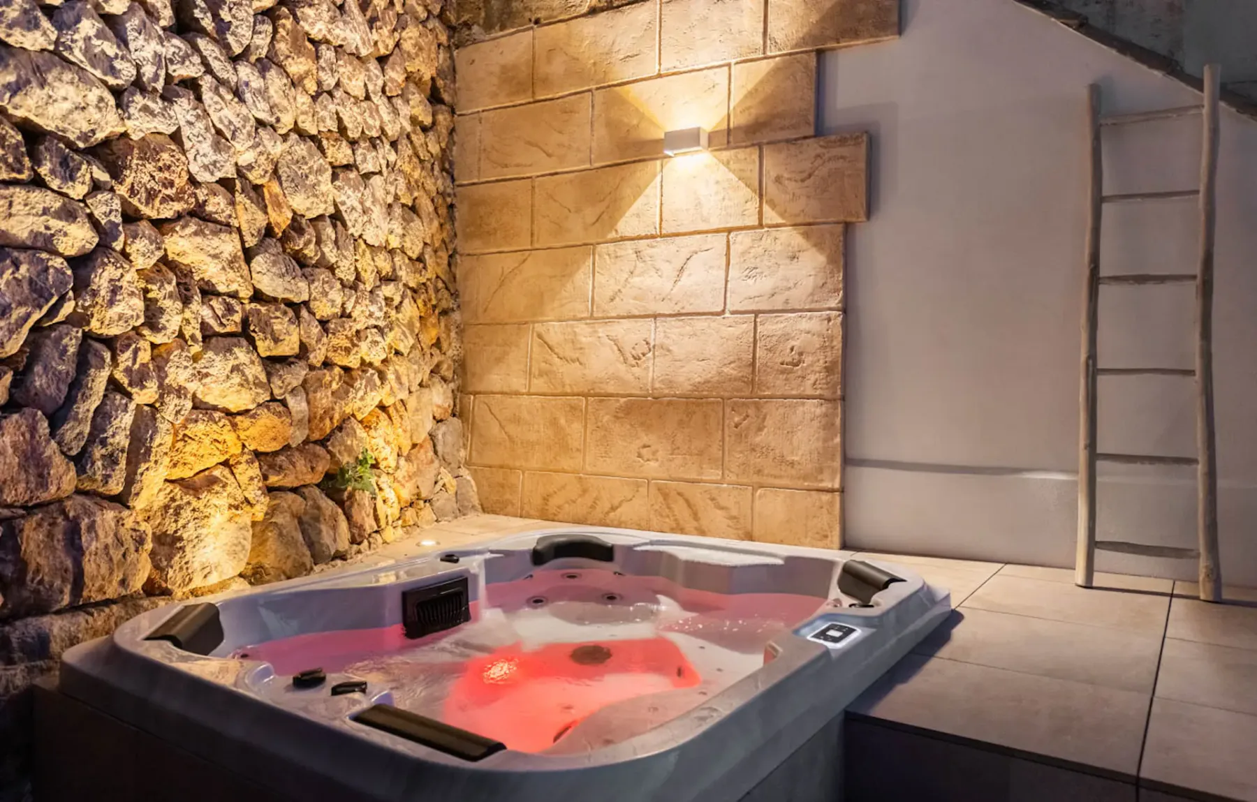 A lit hot tub sits beside stone and tiled walls in an indoor spa area.
