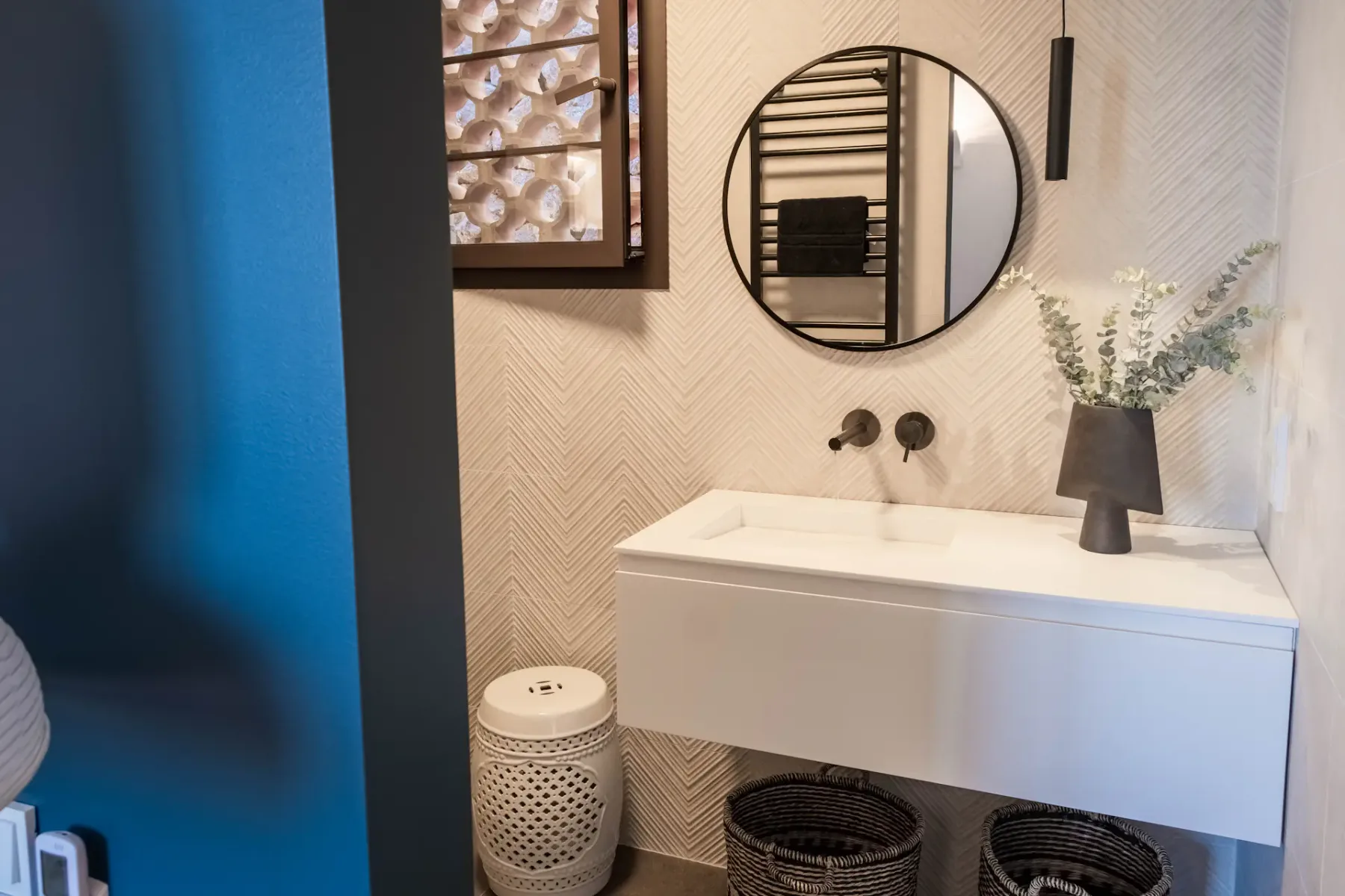 A bathroom vanity with a round mirror and a vase of flowers.